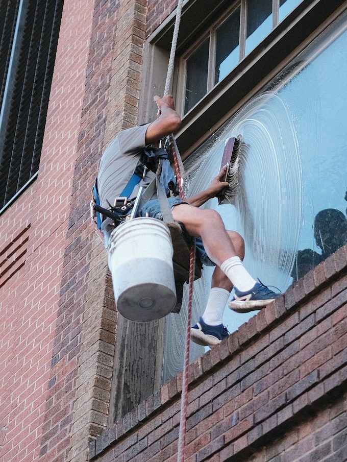 Fensterputzer schwingt sich an Seil und reinigt eine Fensterfläche an einem hohen Gebäude.